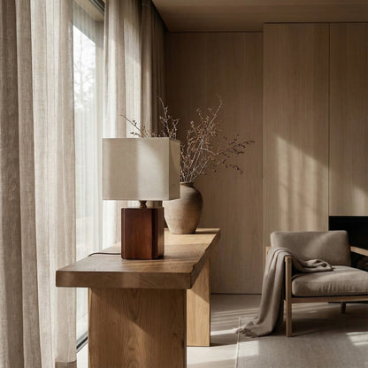 Modern interior with wooden console table, lamp, and chair in a softly lit room.