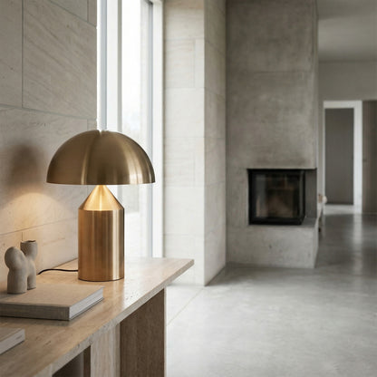 Gold table lamp on a wooden surface in a modern room with concrete walls and a fireplace.