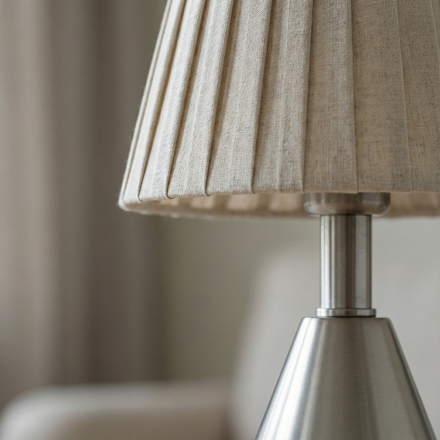 Close-up of a lamp with a beige pleated shade and metallic base.
