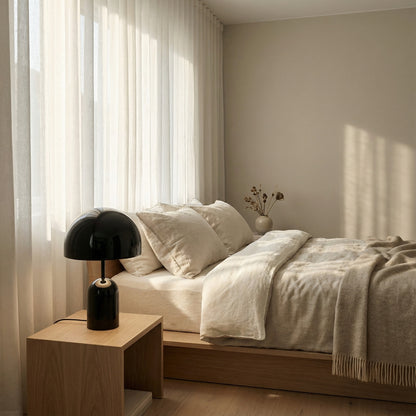 Neatly made bed with white bedding and a beige blanket in a softly lit bedroom.