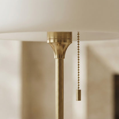 Brass ceiling light fixture with pull chain against a neutral wall.